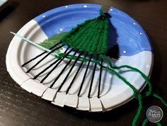 a paper plate with yarn on it and a green christmas tree made out of knitting needles