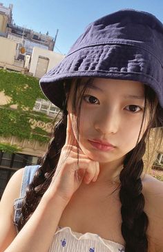 a young woman wearing a blue hat and looking at the camera with her hand on her chin