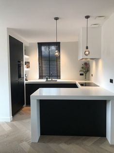 a modern kitchen with black and white cabinets, an island countertop and two pendant lights