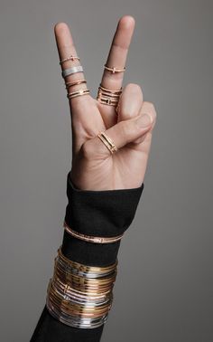 a person making the peace sign with their fingers and rings on each hand, against a gray background