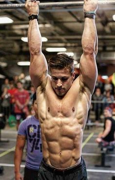 a shirtless man is doing pull ups on a bar in front of other people