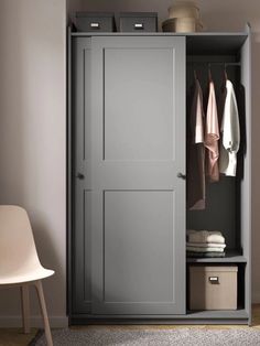 an open gray closet with clothes hanging on the door and two white chairs next to it