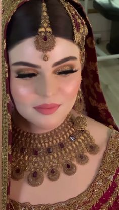 a woman in a red and gold bridal outfit with jewelry on her head, looking at the camera