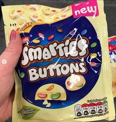 a hand holding a bag of smarties buttons