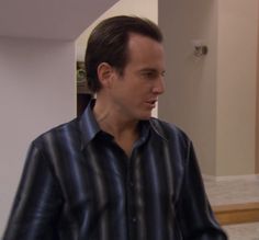 a man wearing a black and blue striped shirt standing in a living room looking off to the side