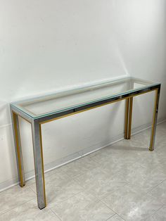 a glass and metal table sitting on top of a tile floor next to a white wall