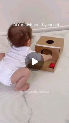 a baby sitting on the floor playing with a cardboard box that has a red ball in it