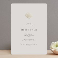 a wedding card with a seashell on it and a flower in the foreground