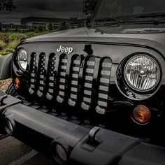 the front end of a black jeep parked in a parking lot with grass and bushes