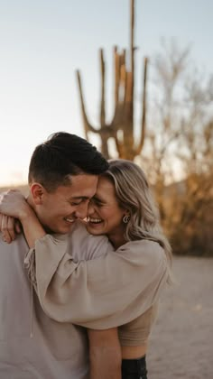 a man and woman hugging each other in front of a saguaya cactus at sunset