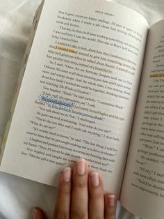 a person is holding an open book in their left hand and reading it on the bed