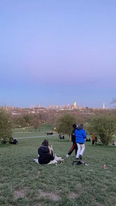 two people are flying a kite in a field with other people sitting on the grass