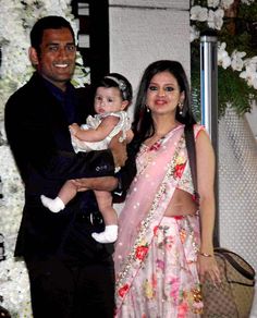 a man holding a baby and standing next to a woman in a pink sari