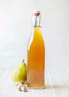 a glass bottle filled with liquid next to a pear