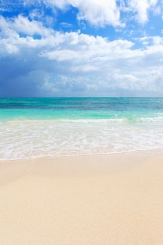 an empty beach with waves coming in to the shore and blue sky filled with clouds