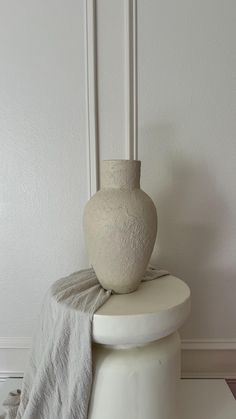 a white vase sitting on top of a table next to a gray cloth draped over it