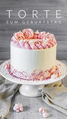 a white cake with pink frosting and sprinkles sitting on top of a table