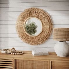 a round mirror hanging on the wall above a wooden table with a lamp and vase