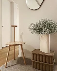 a white vase with flowers sitting on top of a wooden stand next to a mirror