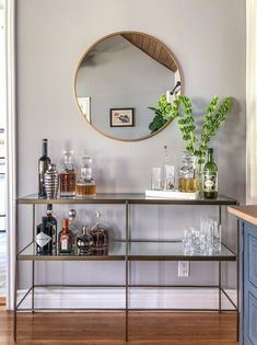 a bar cart with bottles and glasses on it in front of a wall mounted mirror