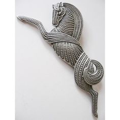 an ornate silver brooch with a lizard on it's back end, sitting on a white surface