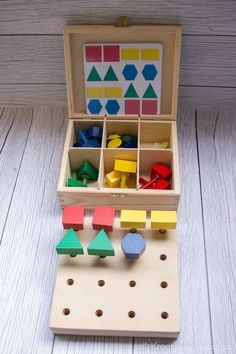 an open wooden box filled with different colored shapes and sizes on top of a white wood floor