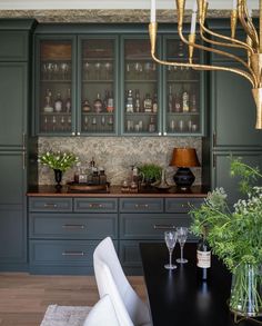 a dining room table with chairs and vases on top of it in front of green cabinets