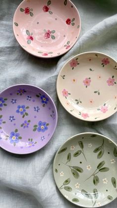 three bowls with flowers painted on them are sitting on a white cloth covered tablecloth