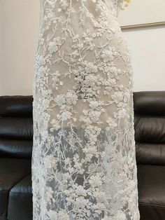 the back of a wedding dress with white flowers on it, in front of a black leather couch