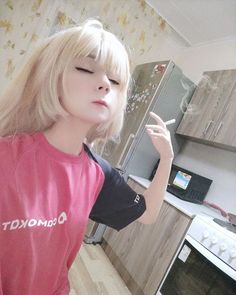 a woman with blonde hair wearing a pink shirt and pointing at something in the kitchen