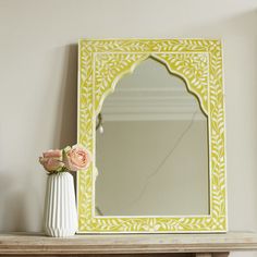 a mirror sitting on top of a wooden shelf next to a vase with flowers in it