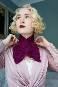 a woman with blonde hair is wearing a purple scarf and has her hands on her neck