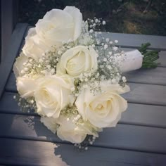 a bridal bouquet with white roses and baby's breath is sitting on a bench