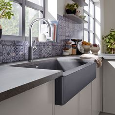 a kitchen sink sitting under a window next to a counter top with potted plants on it