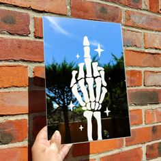 a person holding up a photo of a skeleton hand in front of a brick wall