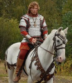 a man in armor riding on the back of a white horse