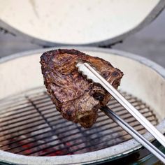 a piece of meat is being grilled on the grill with tongs in it