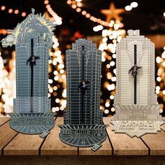 three paper models of skyscrapers on a wooden table with lights in the back ground