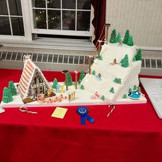 a christmas themed cake is on a red tablecloth in front of a white window