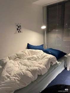 an unmade bed with white sheets and blue pillows in a bedroom next to a window