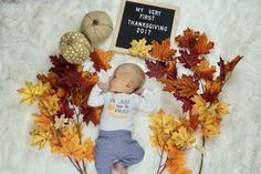 a baby laying on top of a pile of leaves next to a sign that says, my very first thanksgiving 2011