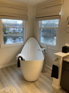 a large bathtub sitting in the middle of a bathroom next to two windows and a sink