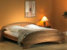 a wooden bed with white sheets and pillows in a room next to a table lamp