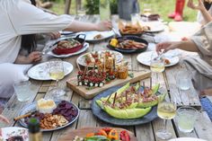 a group of people sitting around a wooden table with plates of food and drinks on it