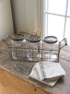 three glass jars sitting on top of a counter next to a white towel and window