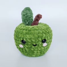 a green stuffed apple with a leaf on it's head and eyes, sitting on a white surface