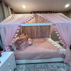 a pink canopy bed with pom poms on the headboard and foot board