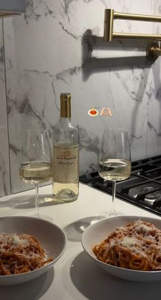 two bowls of spaghetti and wine on a counter