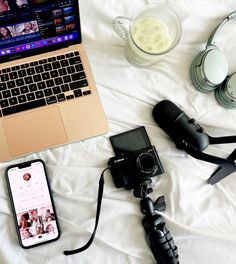 an open laptop computer sitting on top of a bed next to a camera and headphones