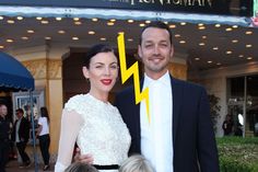 a man and woman standing next to each other in front of a building with a lightning bolt on it